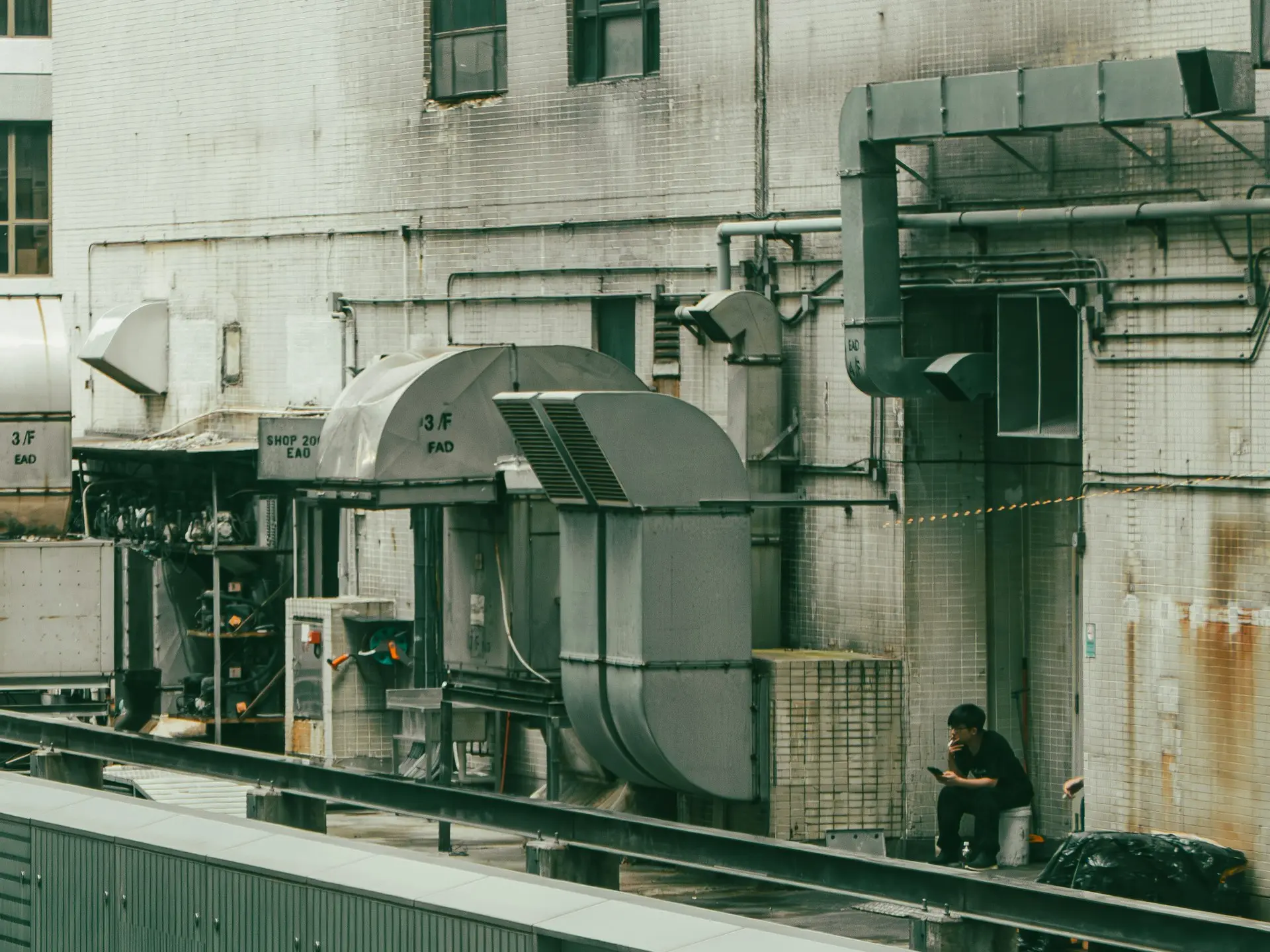 A person sits amidst industrial machinery outdoors.